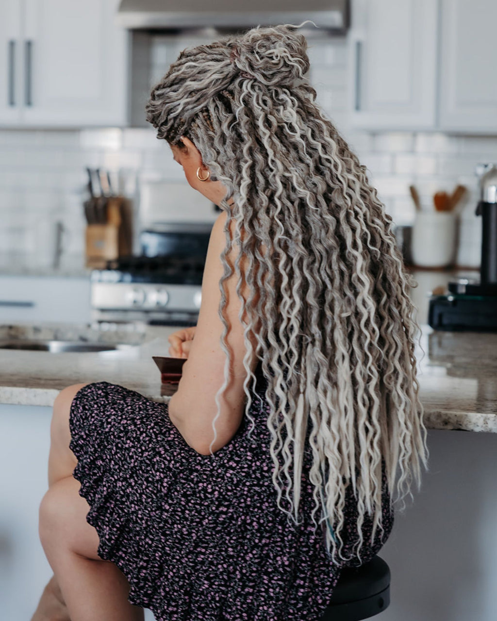 Person with Venus Long Wavy braid-in hair extensions in Smokey Amber color sitting in a kitchen