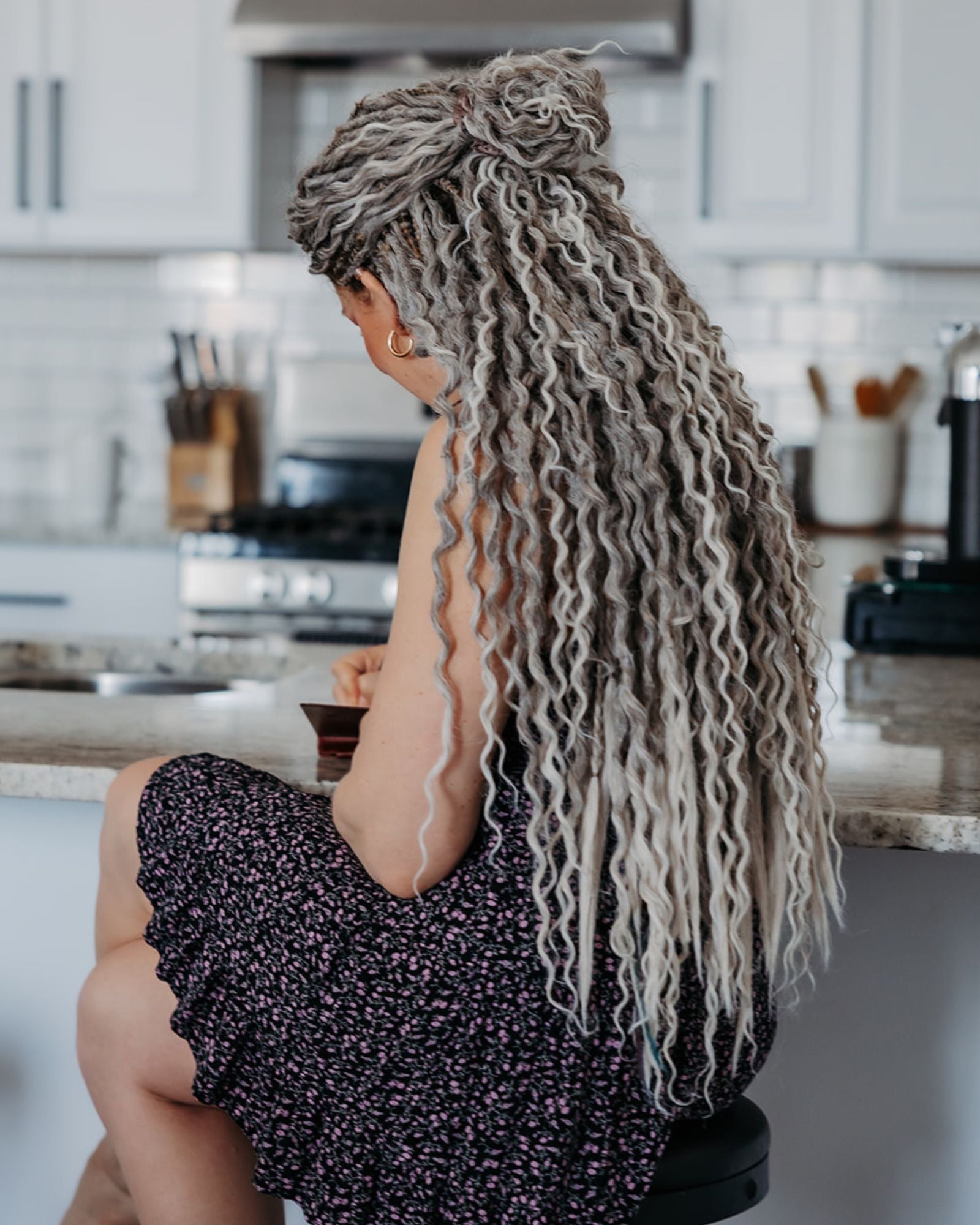 Person with Venus Long Wavy braid-in hair extensions in Smokey Amber color sitting in a kitchen