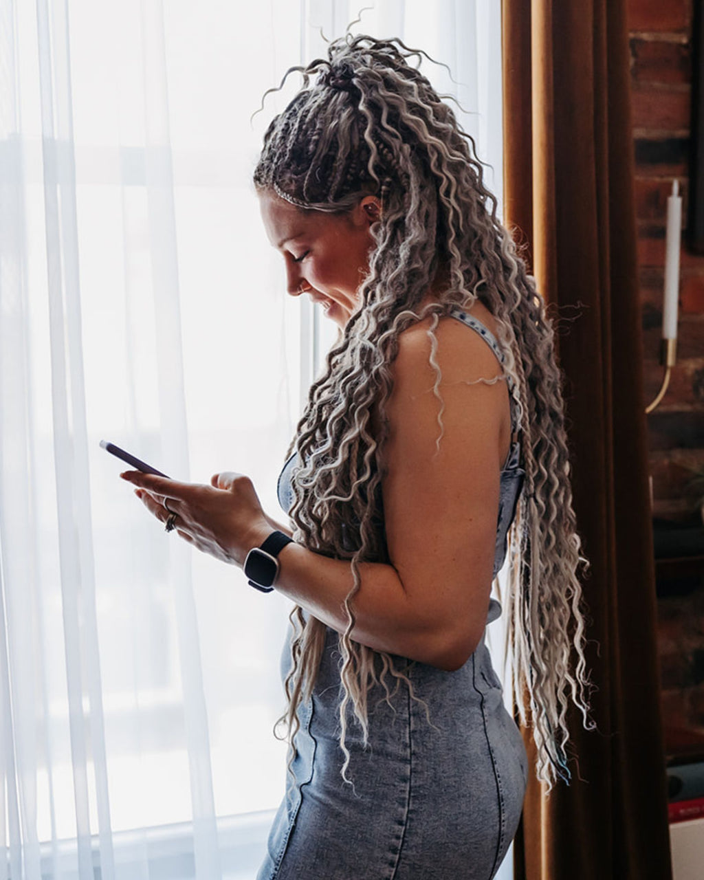 Woman with Venus Long Wavy braid-in hair extensions in Smokey Amber color looking at her phone indoors.