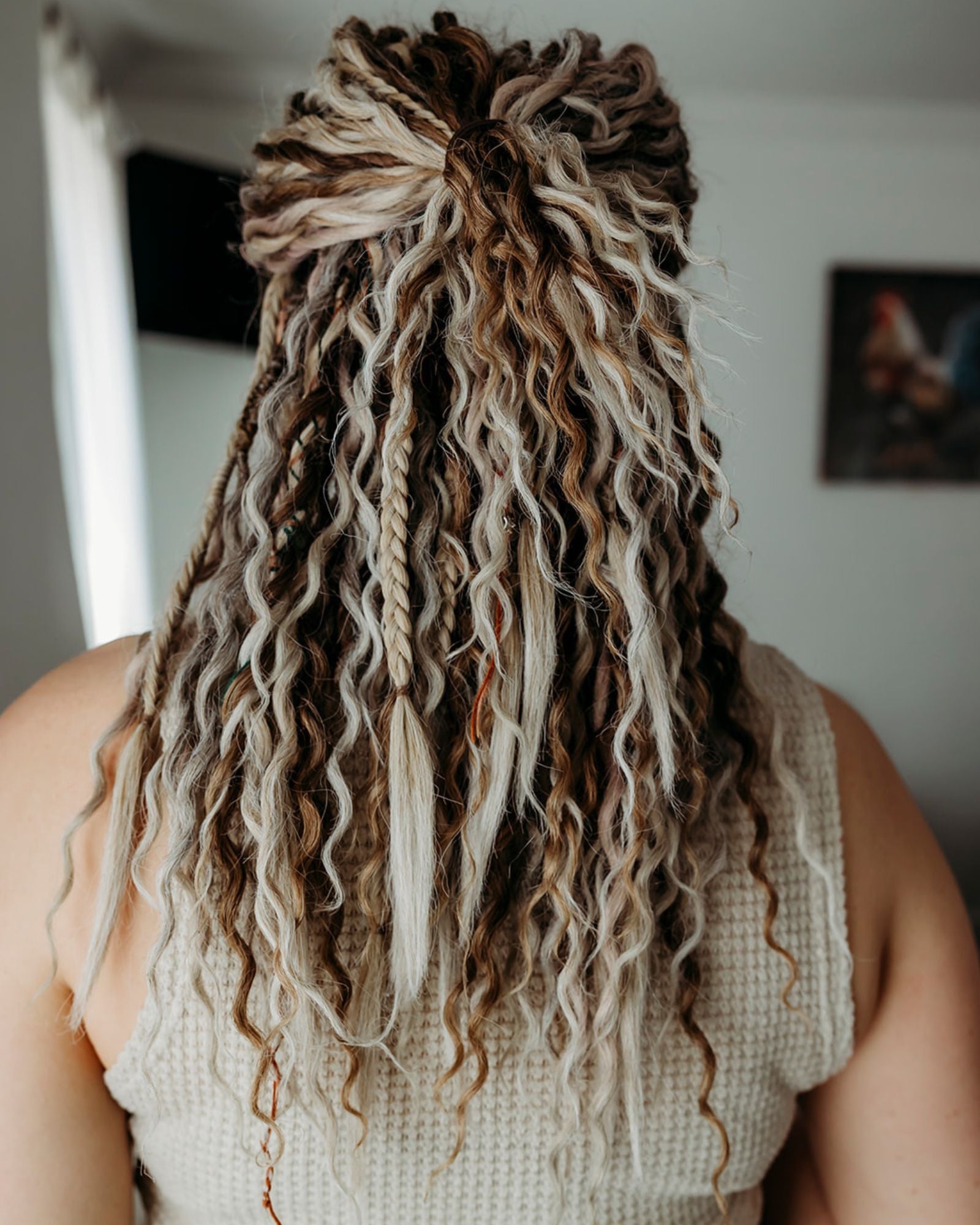 Person with long, styled dreadlocks wearing a beige sleeveless top.