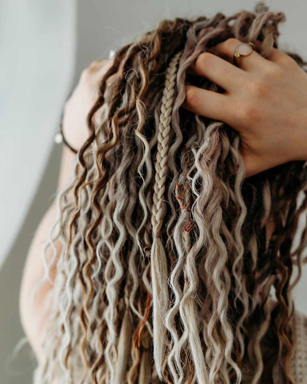 Person with long, wavy hair touching their head against a neutral background