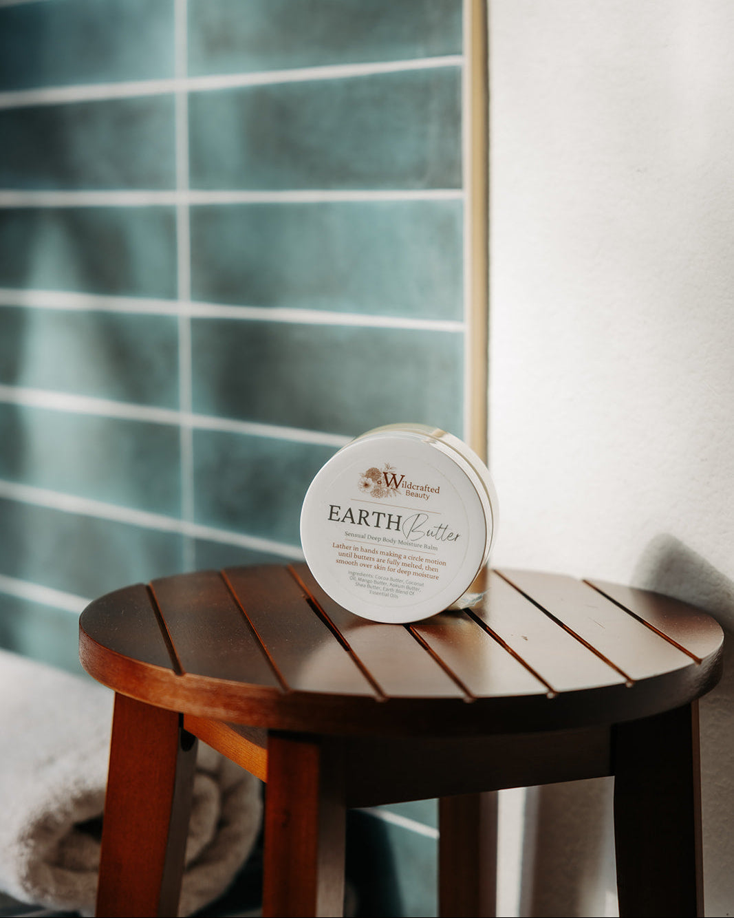 Round container labeled 'Earth Butter' on a wooden stool with a striped wall in the background