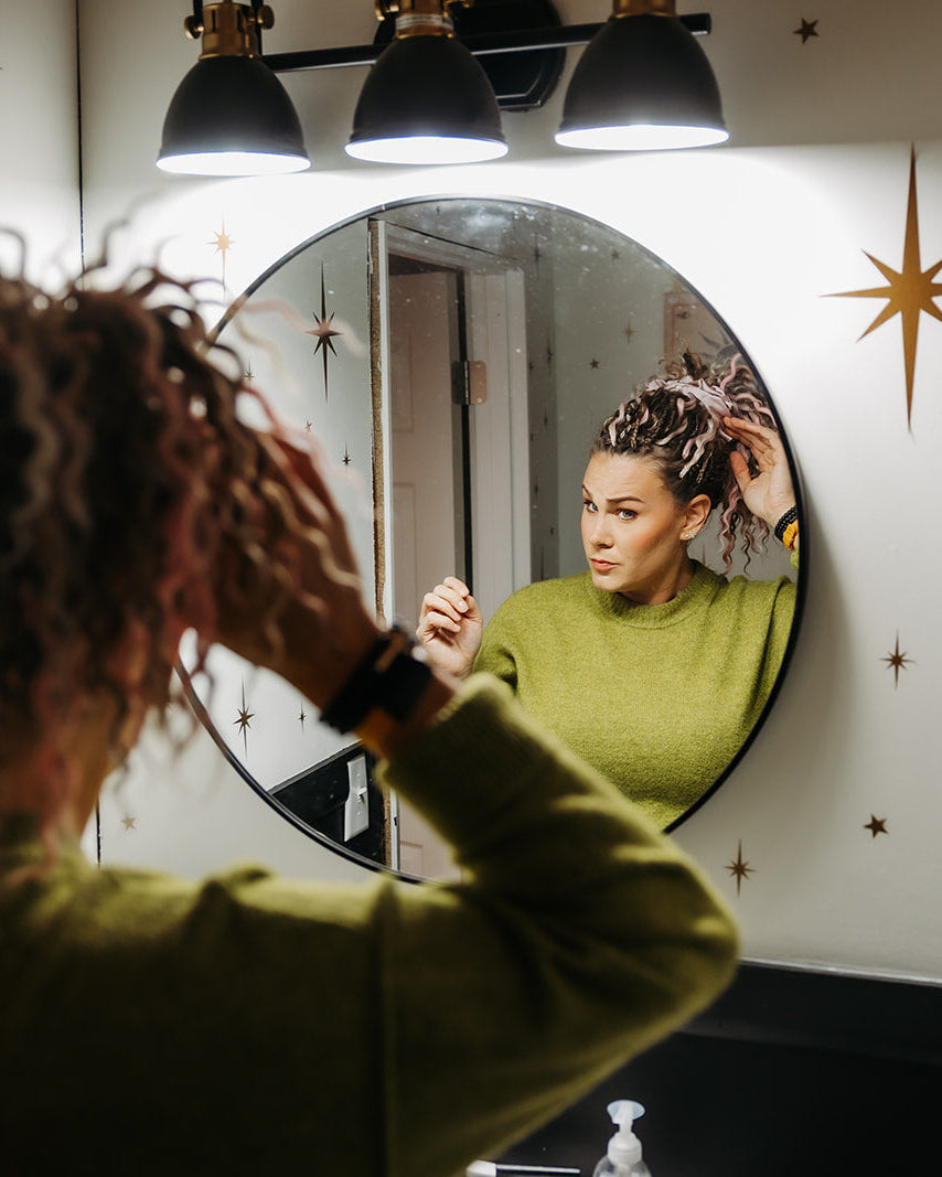 Person styling their hair in front of a round mirror with decorative wall art.