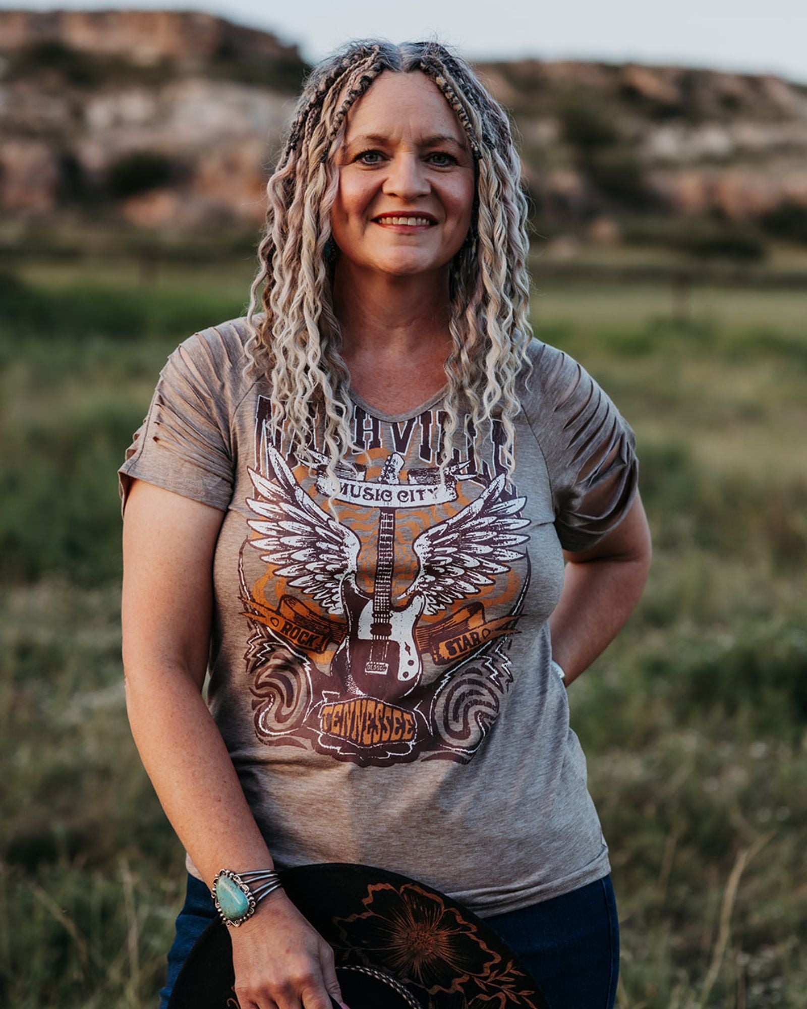 Woman wearing SHORTIES™ Braid-in Extensions with a graphic t-shirt with a guitar design in a natural setting