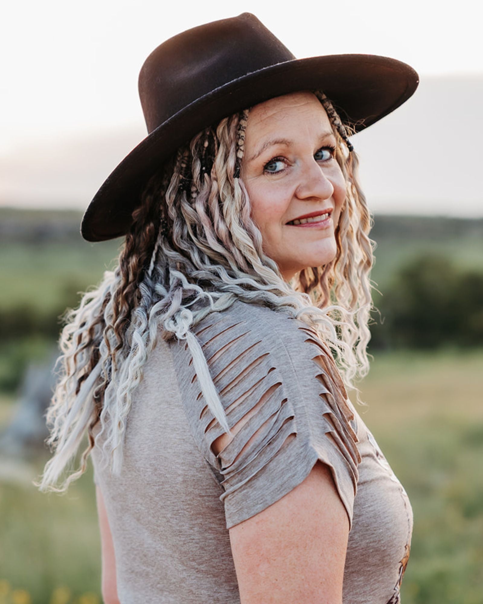 Woman wearing SHORTIES™ Braid-in Extensions with a wide-brimmed hat in an outdoor setting