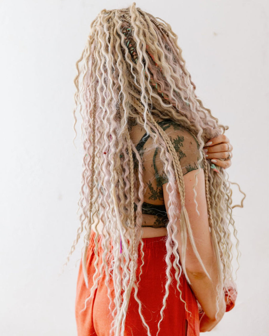 Person with long blonde braided hair and tattoos on a white background
