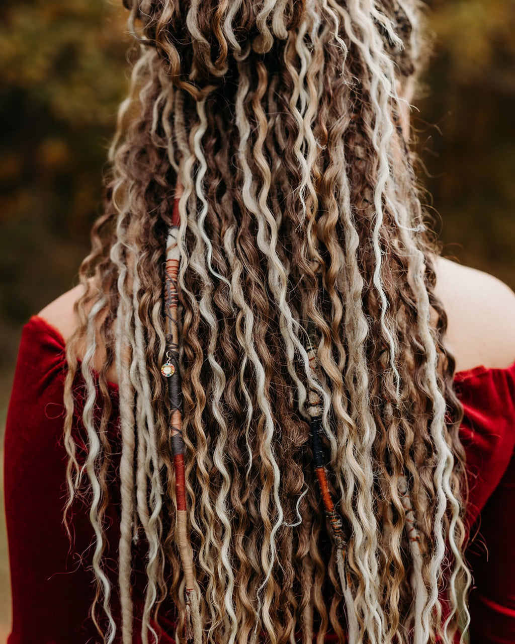 Person with long, wavy hair adorned with beads against a blurred natural background