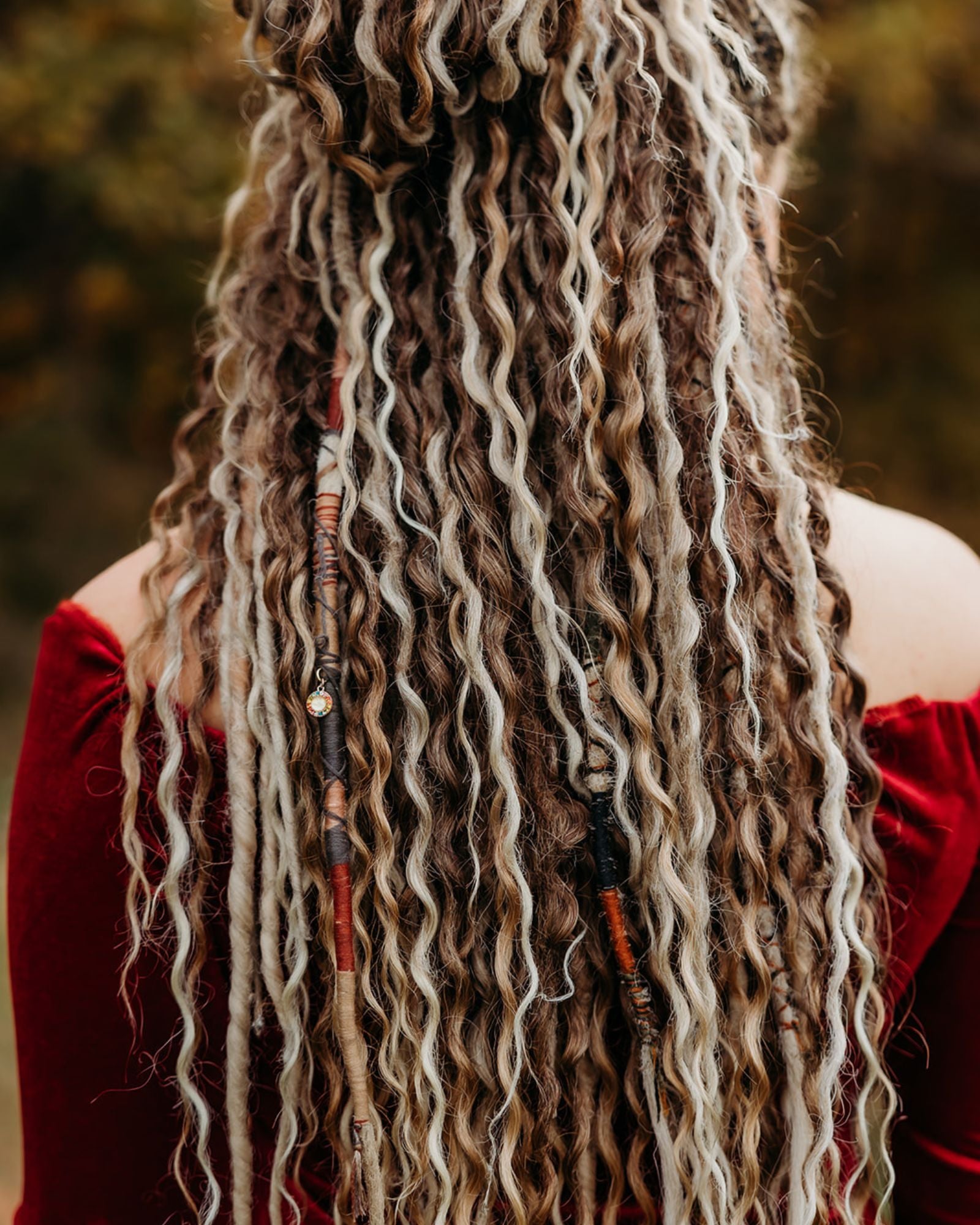 Person with long, wavy hair adorned with beads against a blurred natural background
