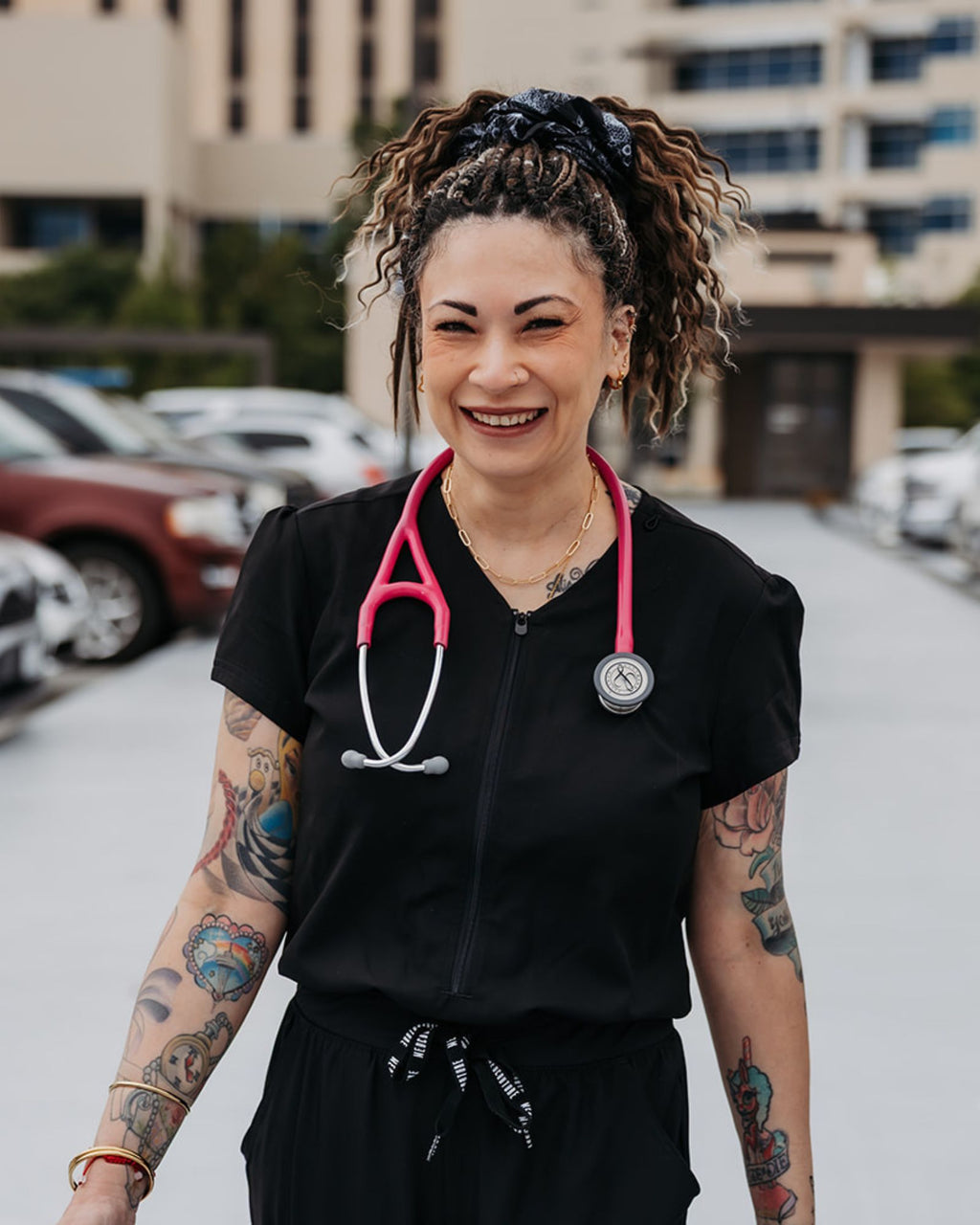 Person wearing SHORTIES™ Braid-in Hair Extensions and a black outfit with a pink stethoscope, standing outdoors.