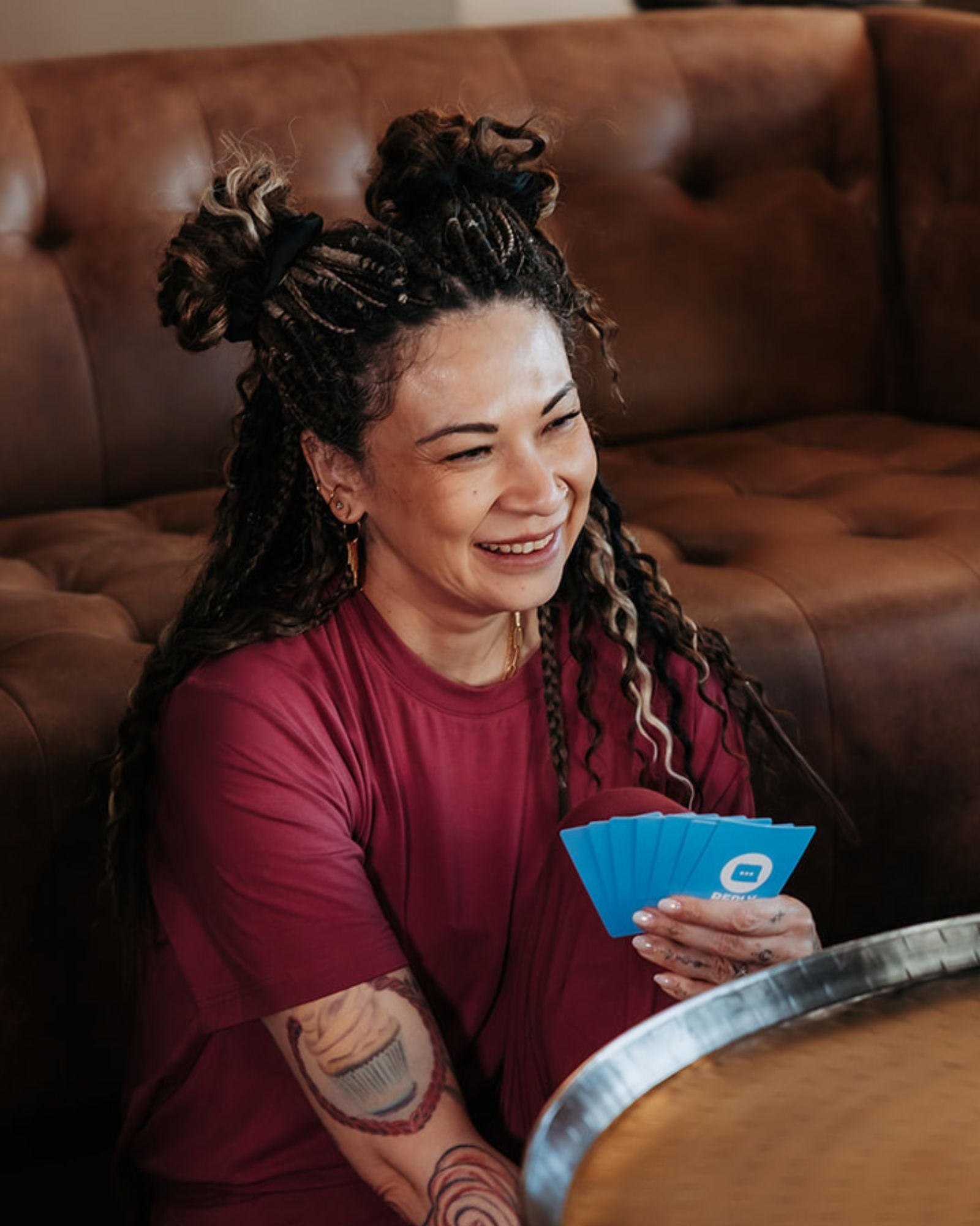 Woman with SHORTIES™ Braid-in Hair Extensions sitting on a brown couch holding blue cards.