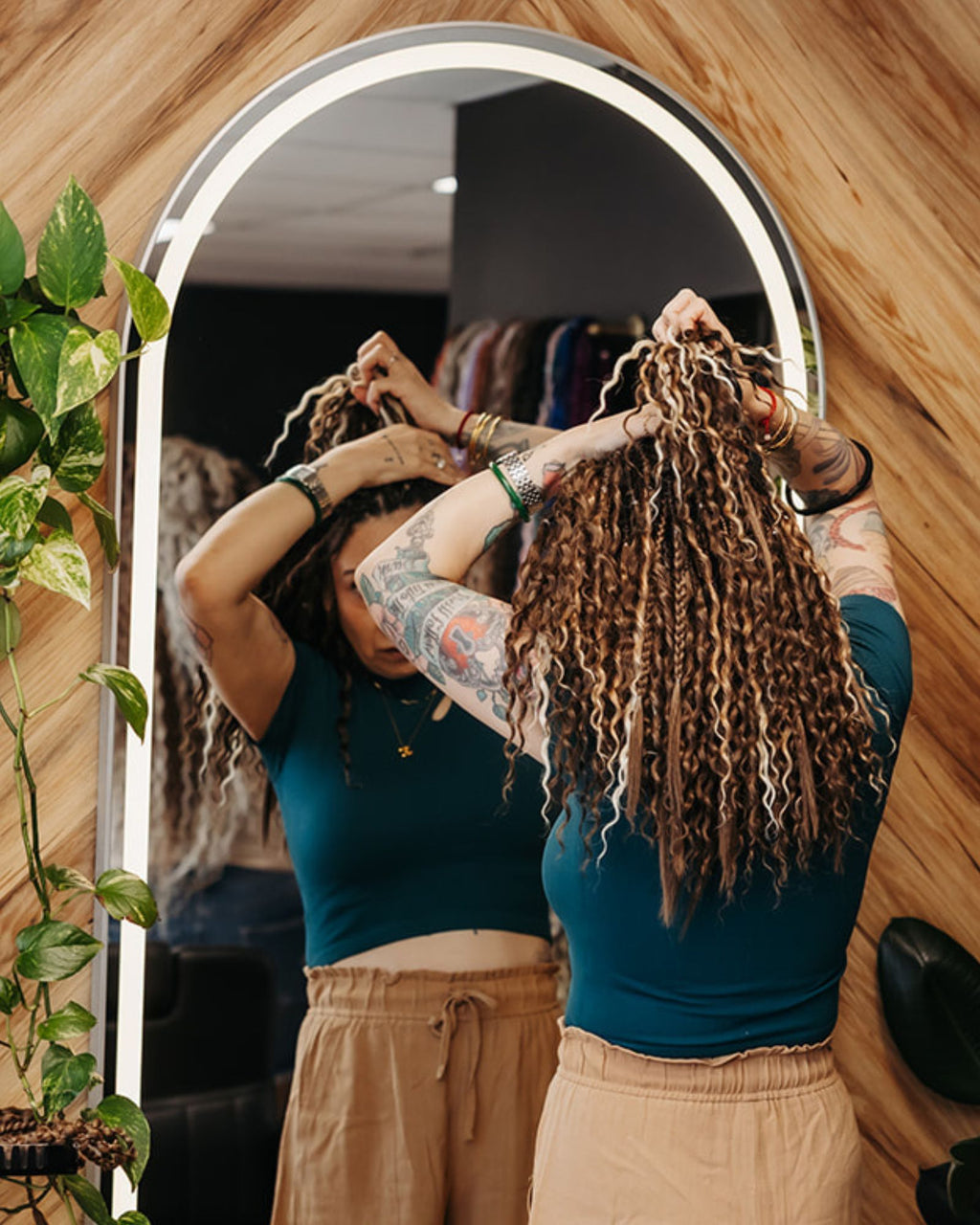Person styling their SHORTIES™ Braid-in Hair Extensions in front of a mirror with a wooden wall background