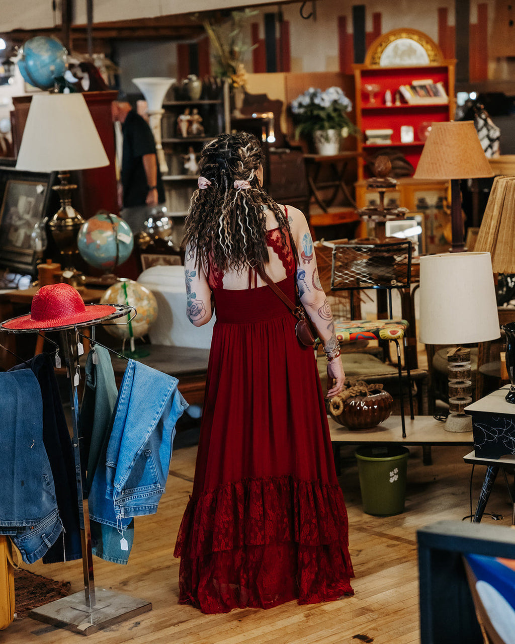 Woman wearing SHORTIES™ Braid-in Hair Extensions in a red dress standing in a store with various items on display.