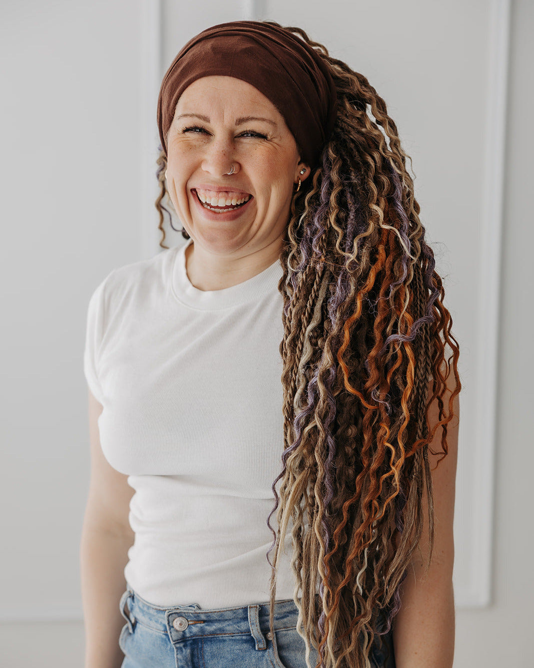 Woman with Venus Long Braid-in Hair Extensions wearing a brown headscarf and white shirt against a white background