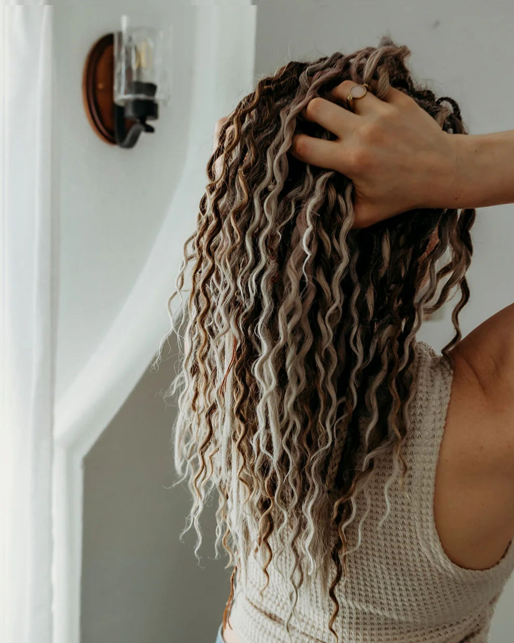 Person with SHORTIES™ braid-in Hair extensions adjusting it in a neutral indoor setting