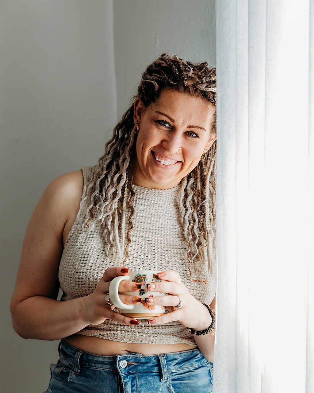 Woman with SHORTIES™ braid-in Hair extensions holding a mug, standing indoors with a neutral background