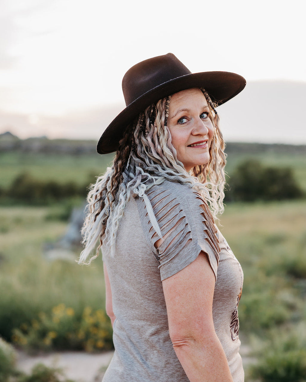 Woman wearing a brown hat and gray top standing in a field with a blurred background