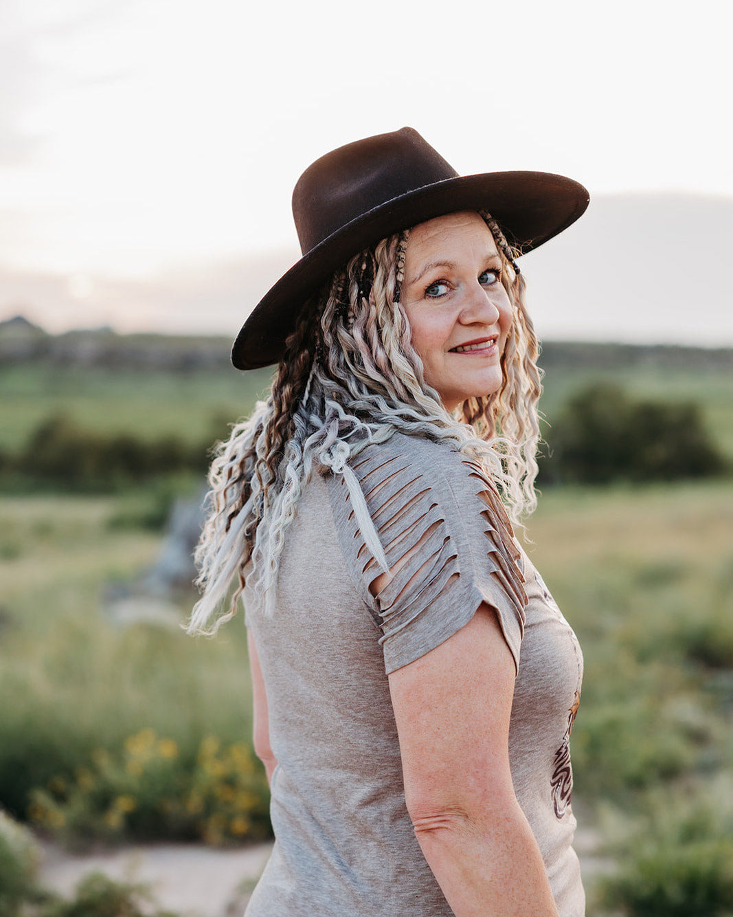 Woman wearing a brown hat and gray top standing in a field with a blurred background
