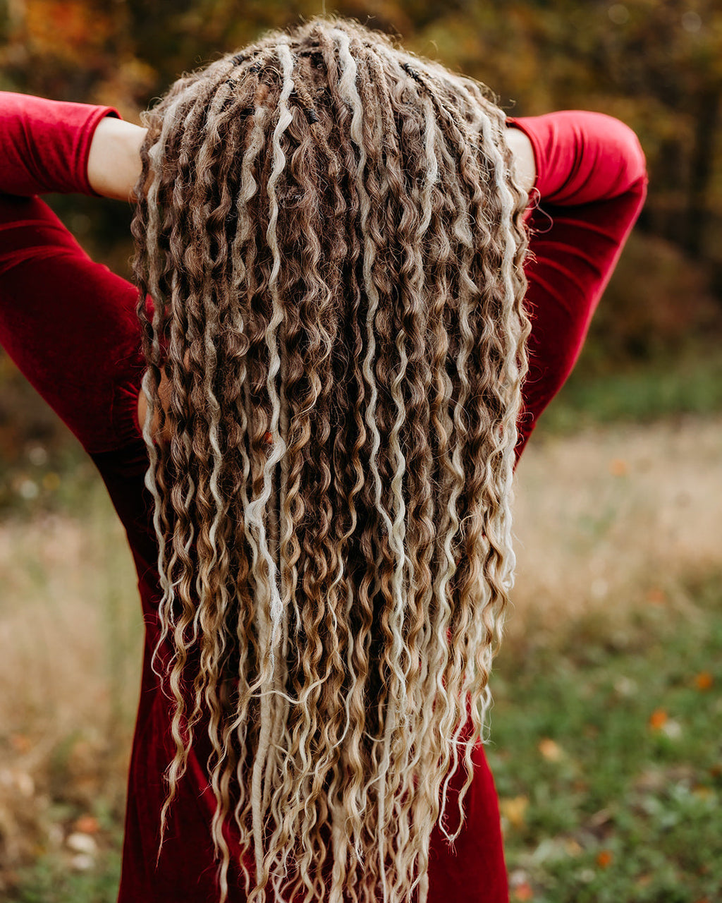 Person with Venus Long Braid-in Hair Extensions standing in a field with blurred autumn trees in the background