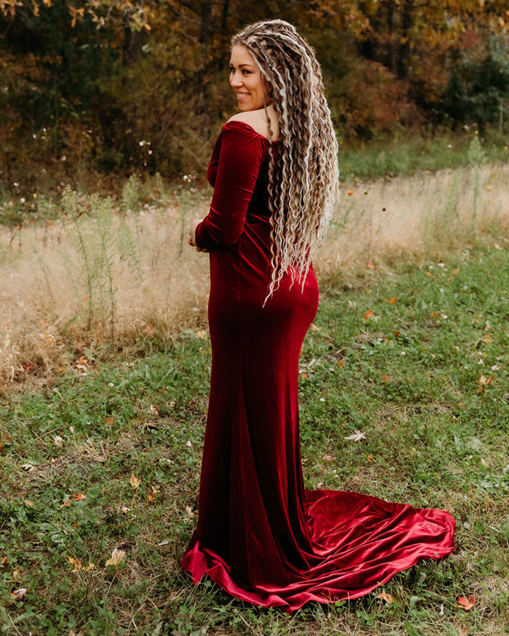 Woman wearing Venus Long Braid-in Hair Extensions in a red velvet dress standing in a natural setting with trees and grass.
