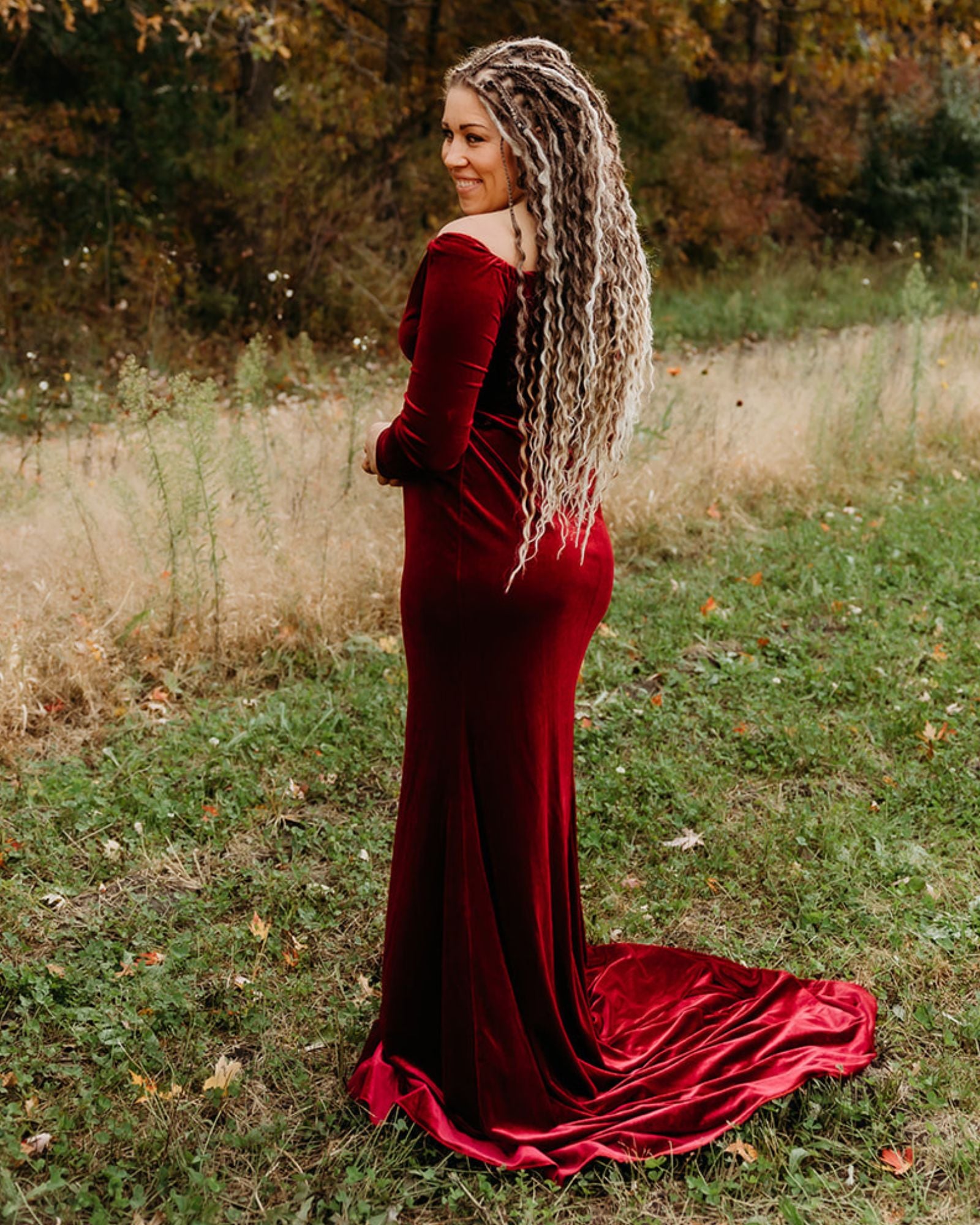 Woman wearing Venus Long Braid-in Hair Extensions in a red velvet dress standing in a natural setting with trees and grass.