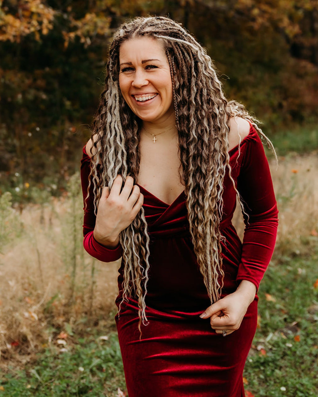 Woman in a red velvet dress with Venus Long Braid-in Hair Extensions standing in a natural setting.