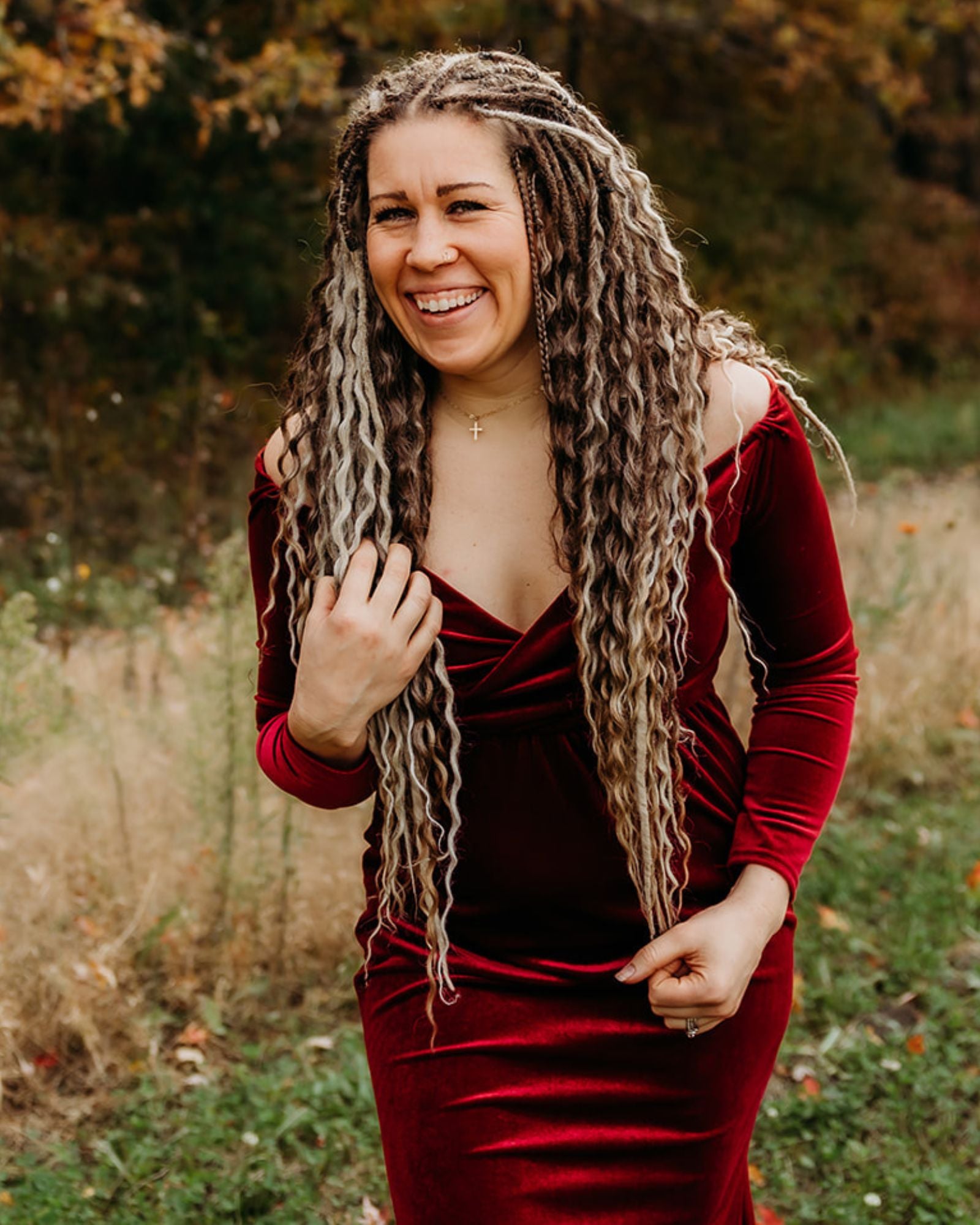 Woman in a red velvet dress with Venus Long Braid-in Hair Extensions standing in a natural setting.
