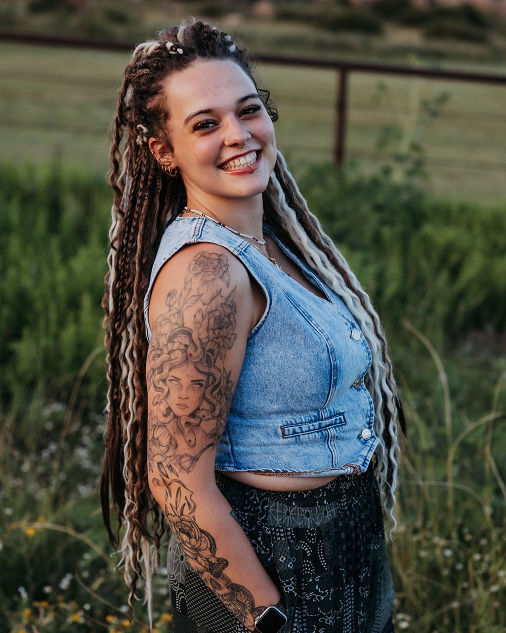 Woman with Venus Long braid-in Hair extensions and tattoos wearing a denim vest in a natural setting