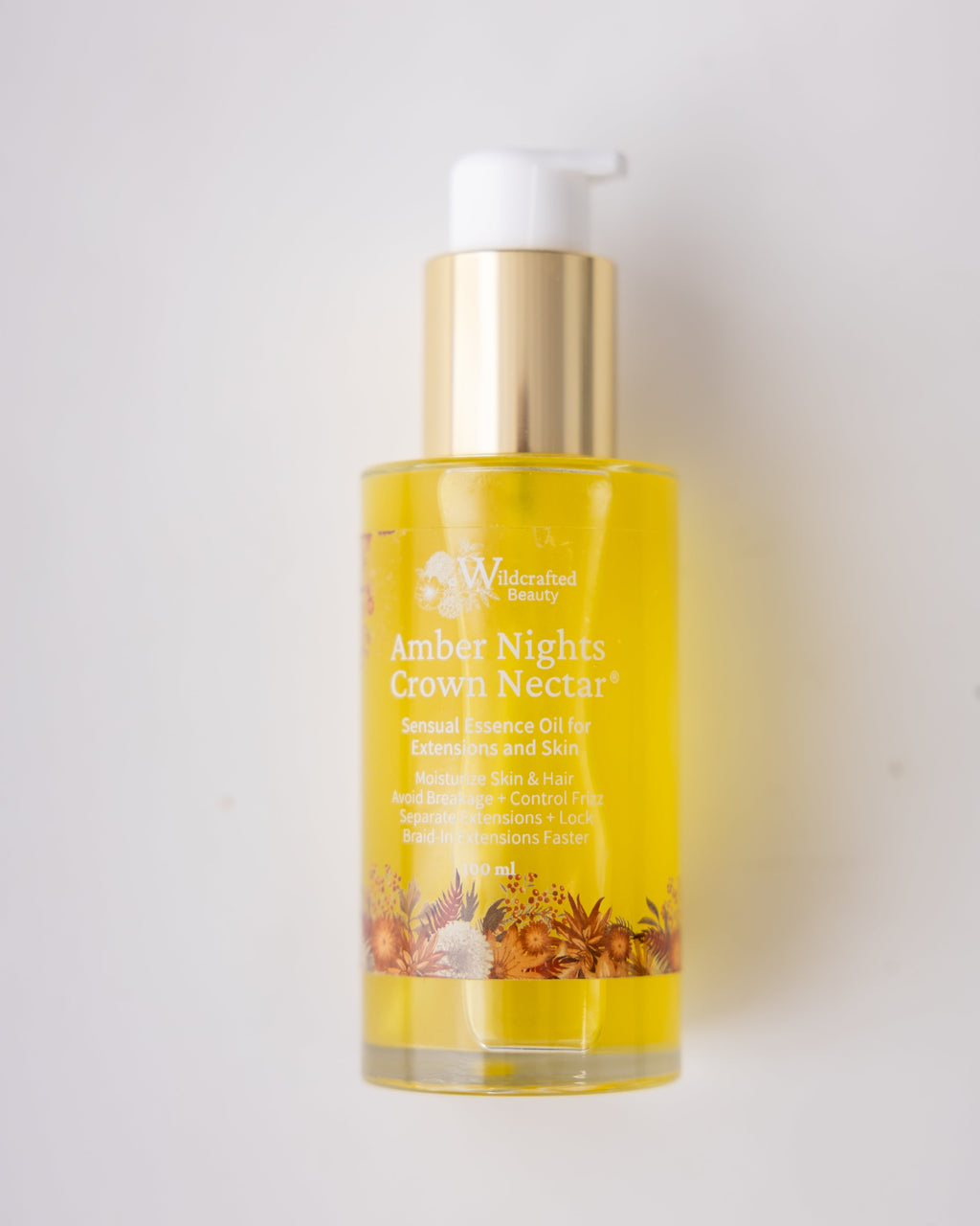 A bottle of Wildcrafted Beauty Amber Nights Crown Nectar, featuring a gold pump dispenser and a clear bottle showing the golden-yellow oil inside, set against a plain white background.