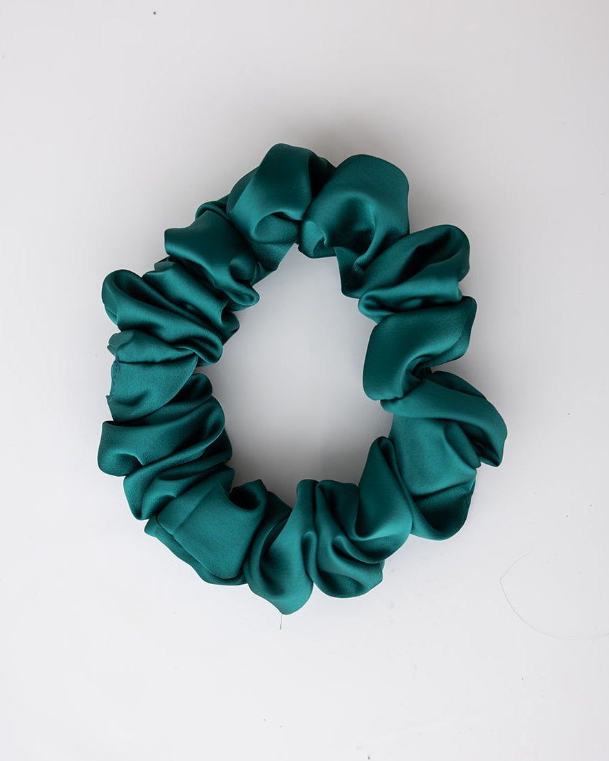 A dark teal green satin hair scrunchie centered on a plain white background.