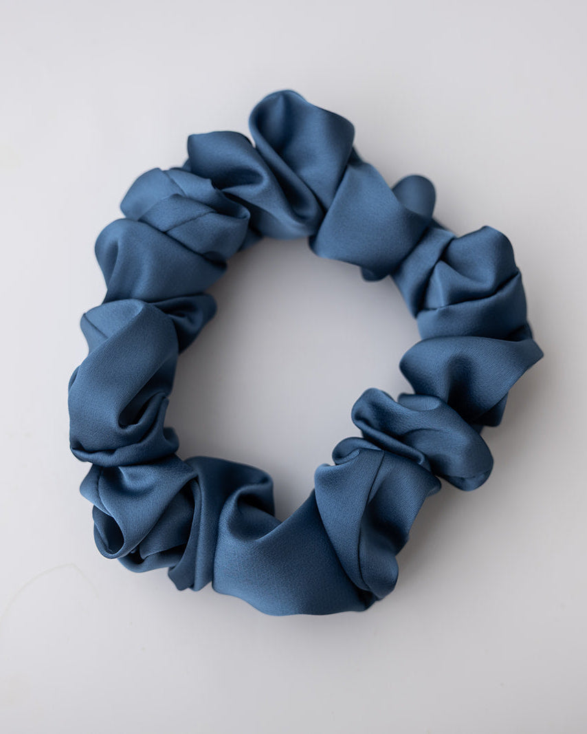 A single dark blue satin scrunchie with a soft, gathered texture, photographed from above on a clean white background.