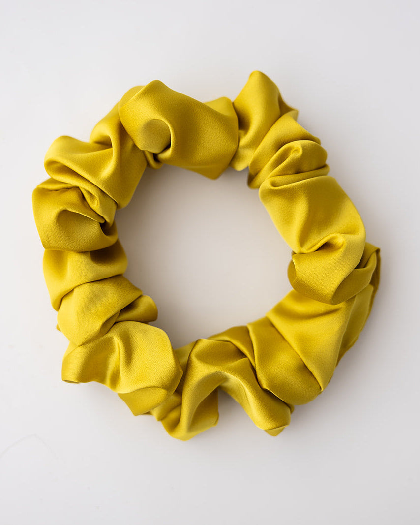 A single yellow satin scrunchie photographed from above on a plain white background.