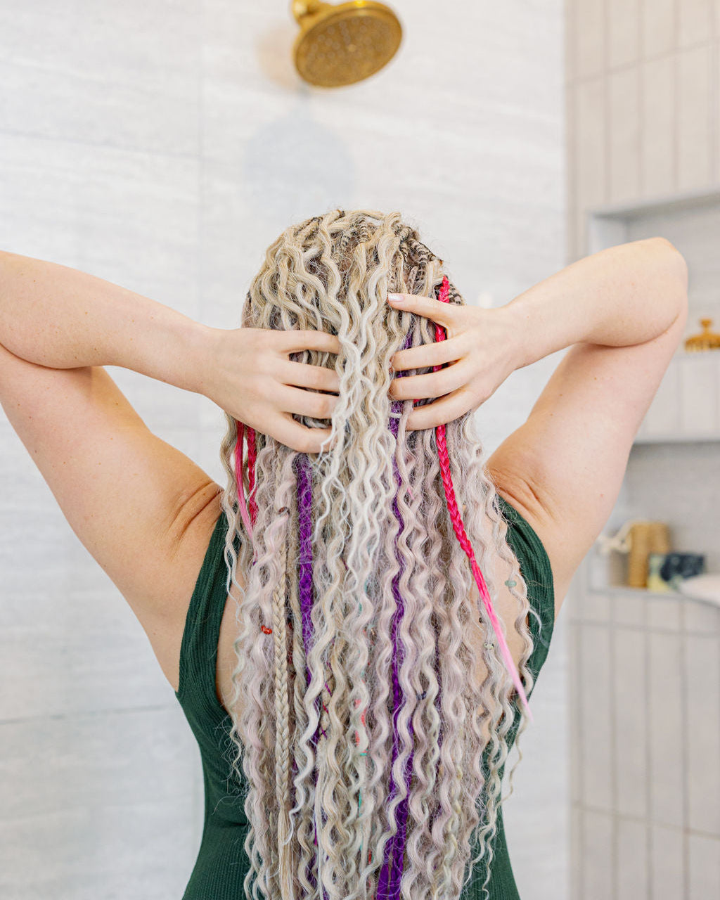 Girl with long WCB extensions in a white tiled shower with her hands in her extensions.