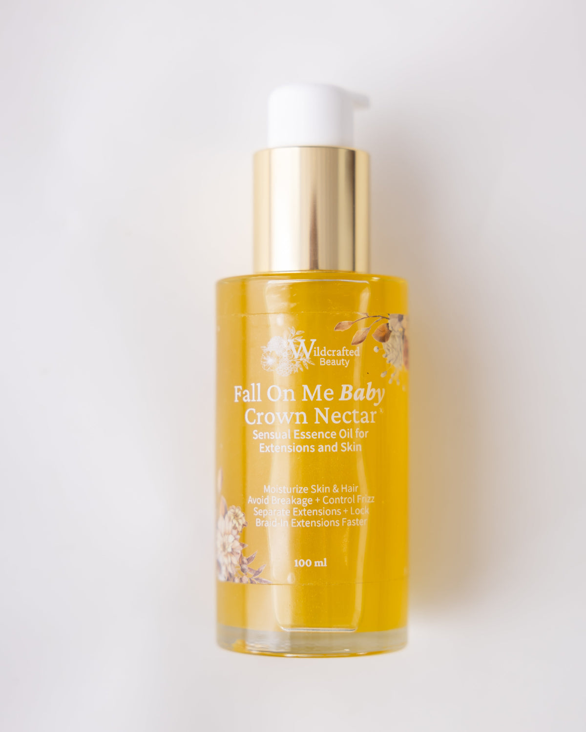 A 100ml bottle of Wildcrafted Beauty 'Fall On Me Baby Crown Nectar' serum essence oil. The bottle is filled with golden-yellow oil and features a shiny gold pump dispenser with a white cap, set against a clean white background.
