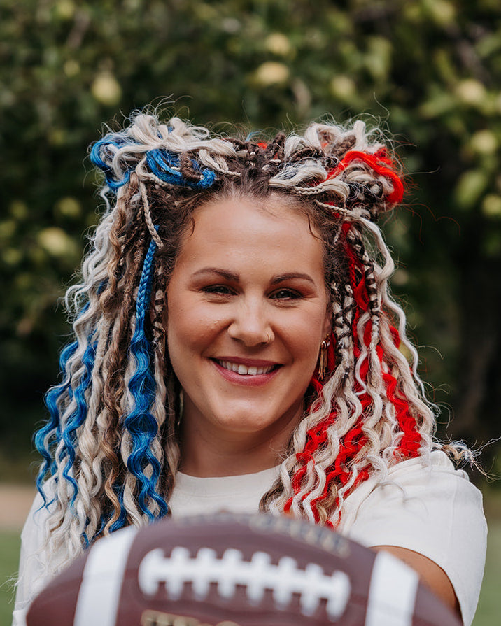 Girl in blonde, blue and red braid-in extensions outdoors holding a football.