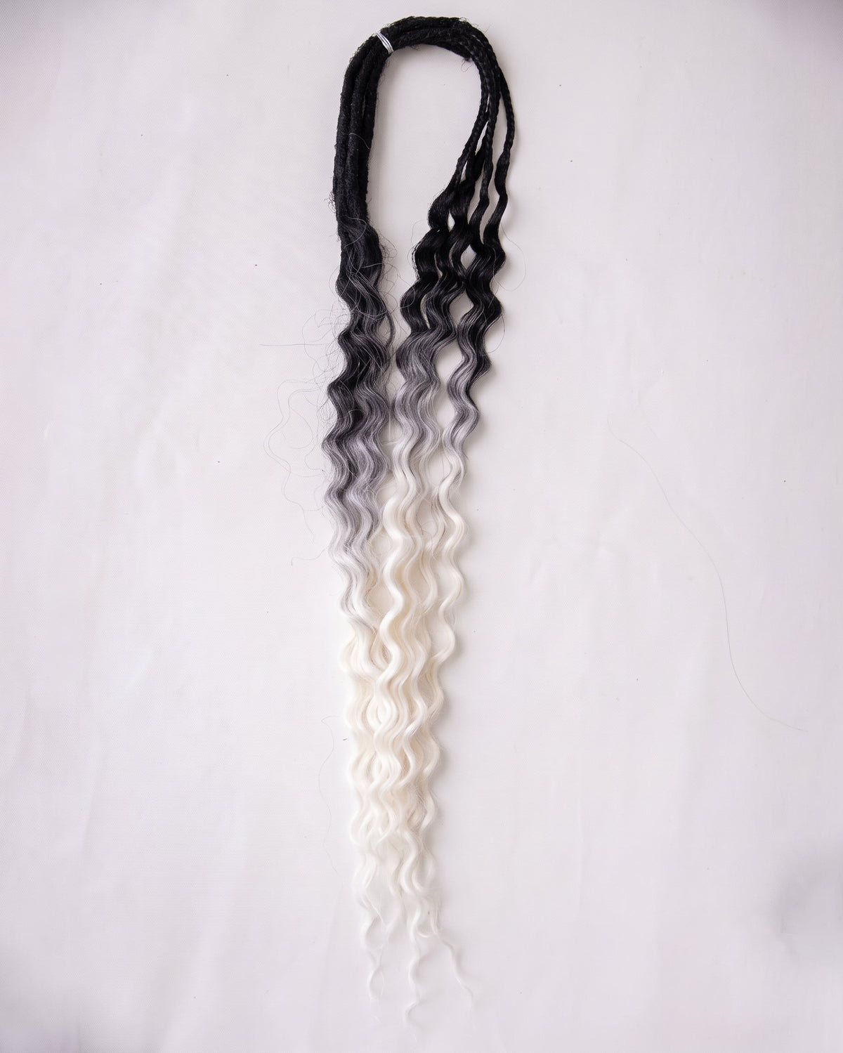 A long, wavy synthetic braided hair extension with a black-to-white ombré color gradient, displayed against a plain white background.