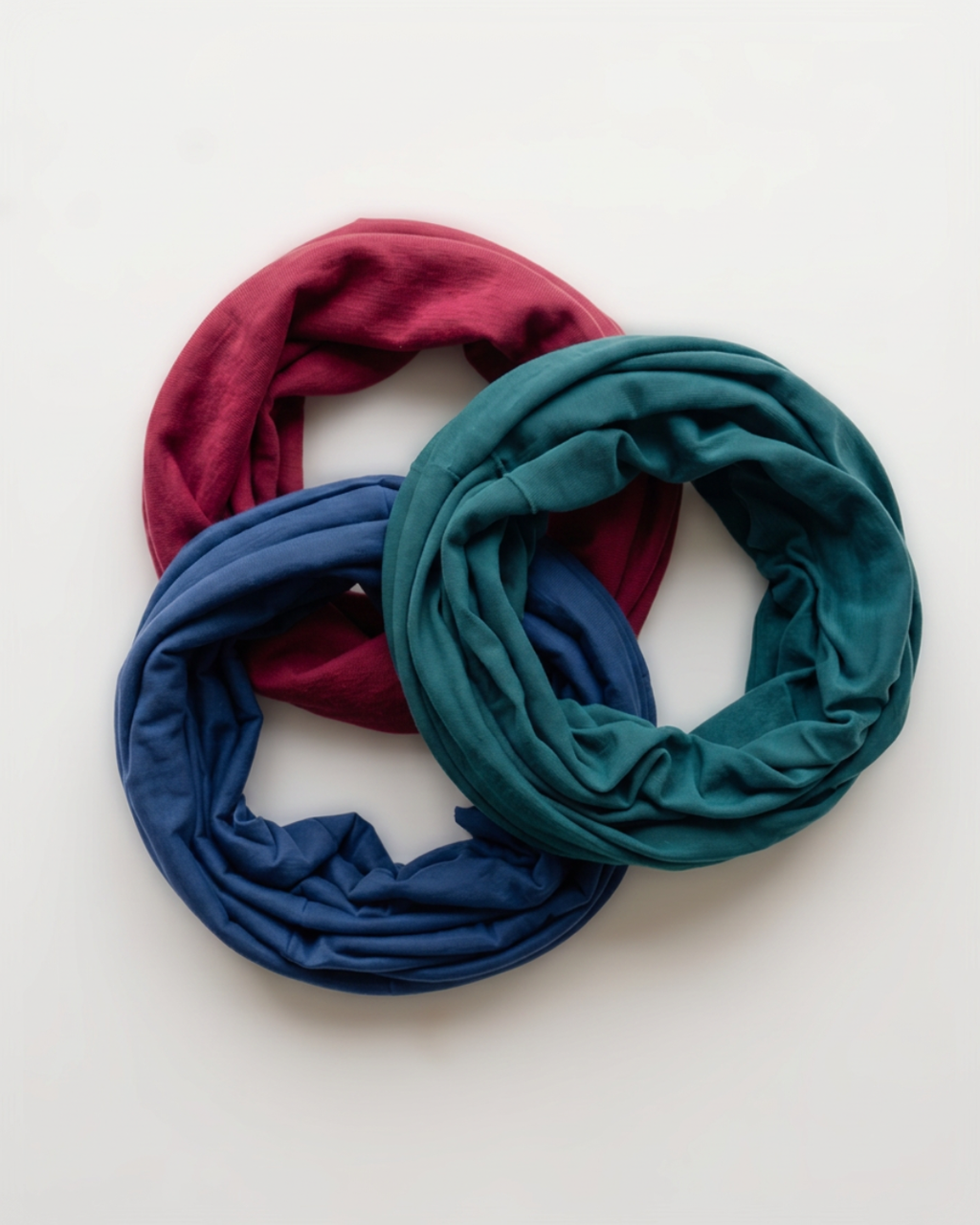 Three headbands in overlapping loops, displayed on a clean white background. The headbands are in three distinct colors: a deep magenta, a teal green, and a royal blue.