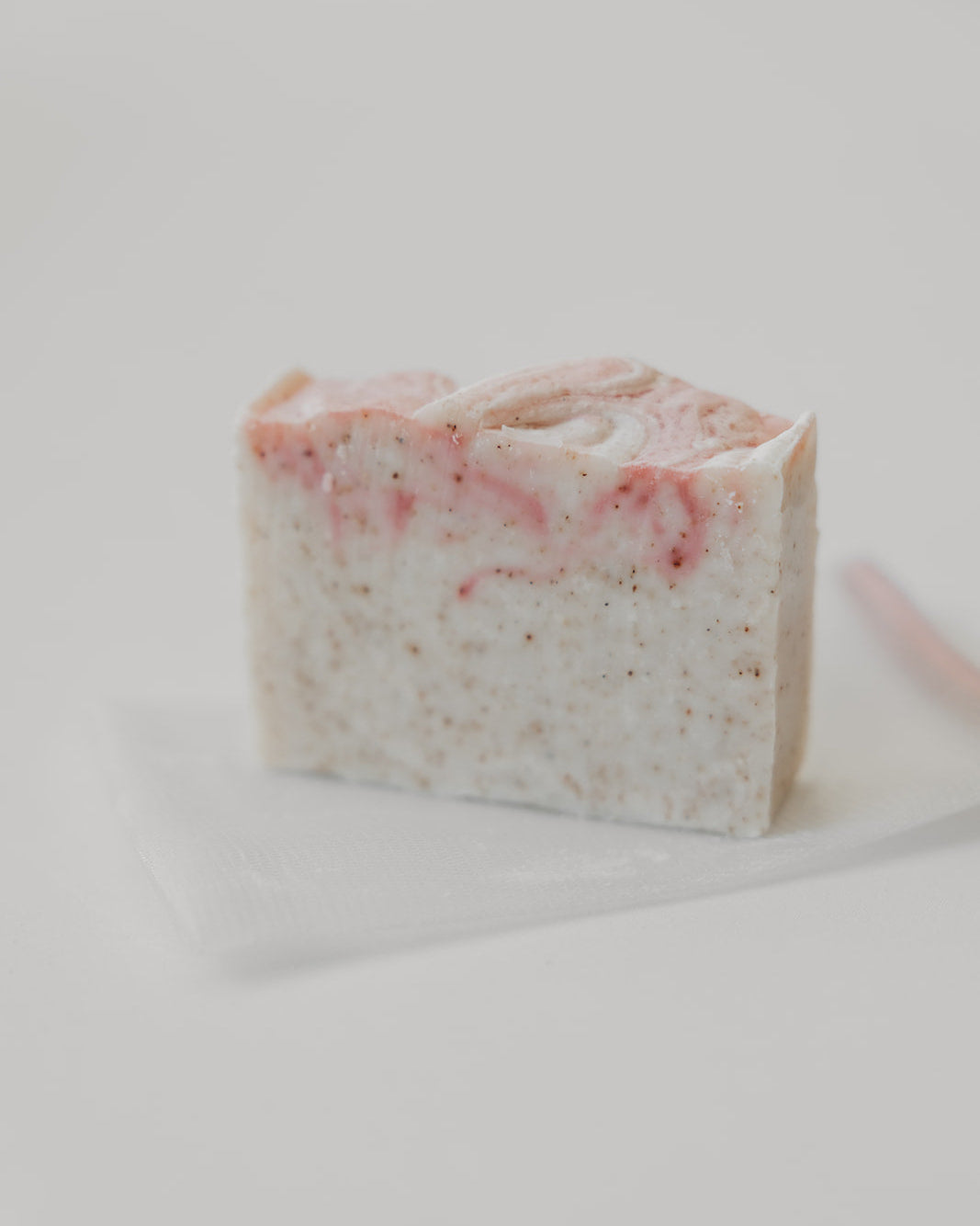 A single rectangular bar of handmade soap with pink swirls and speckled texture, resting on a translucent sheet against a plain light background.