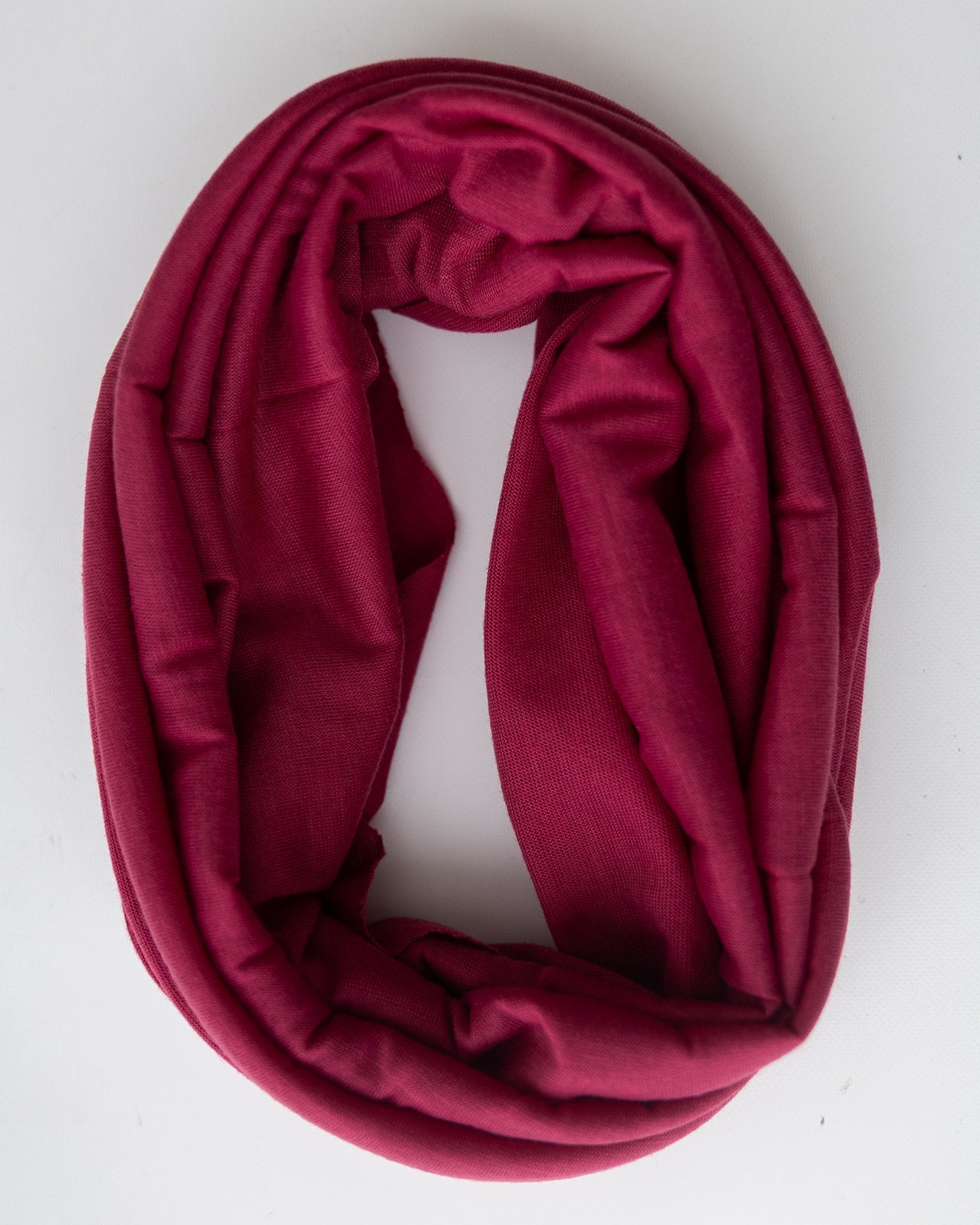 A berry red head band, folded and arranged in a loop on a plain white background.