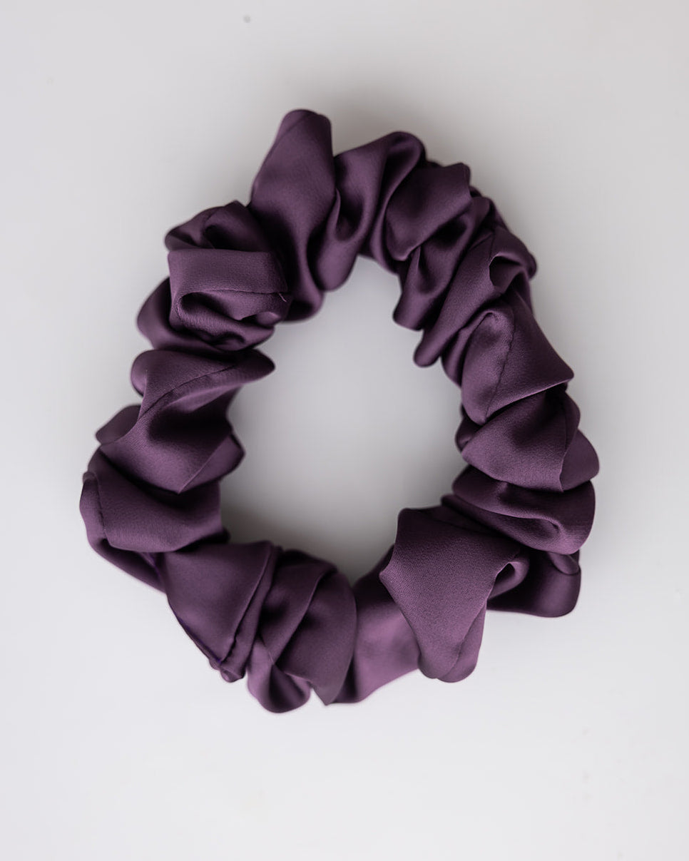 A dark purple satin scrunchie with a ruffled texture, photographed on a clean white background.