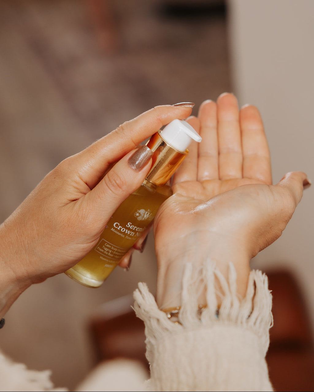 A close-up of a person's hands holding a gold bottle of Serenity Crown Nectar and dispensing the oil into the other hand, with a warm, blurred indoor background.