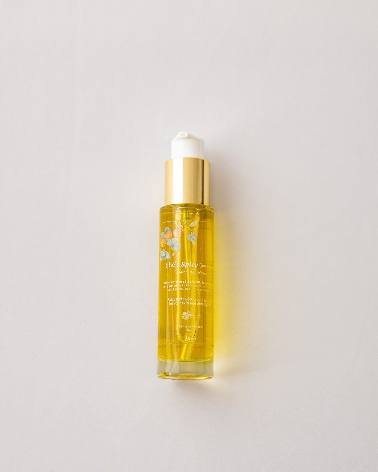A clear glass bottle of WCB's She's Spicy filled with golden yellow liquid, featuring a shiny gold collar and a white pump cap, set against a plain light gray background.