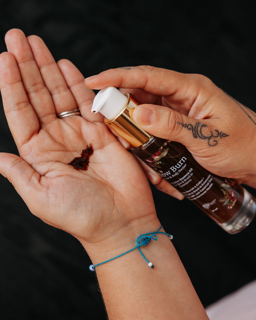 A close-up of a person's hands dispensing a dark amber liquid from a bottle labeled 'Hair Bliss' onto their palm, set against a dark textured background.
