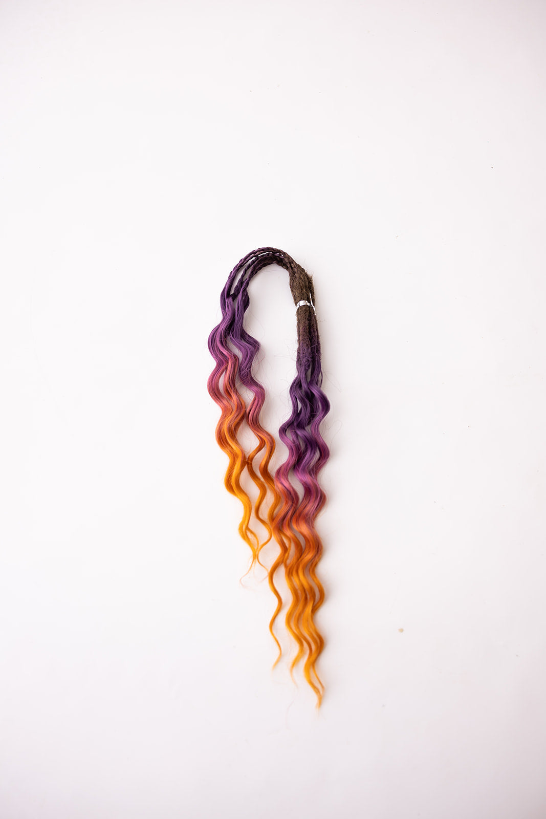 A single synthetic wavy hair extension bundle with a dark brown root transitioning into purple, pink,  and orange, shown against a plain white background.