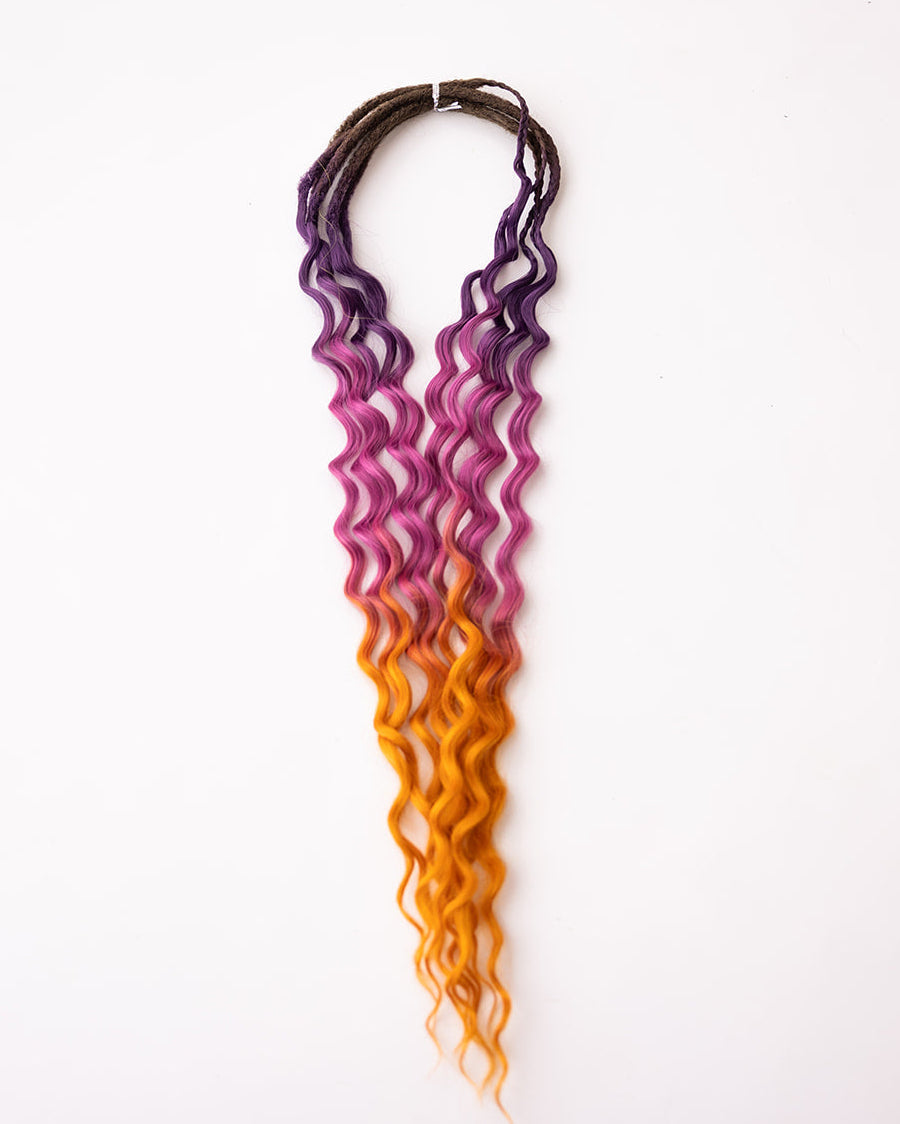 A long, wavy synthetic hair extension with a four-color ombre gradient transitioning from dark brown to purple to pink to orange, shown against a plain white background.