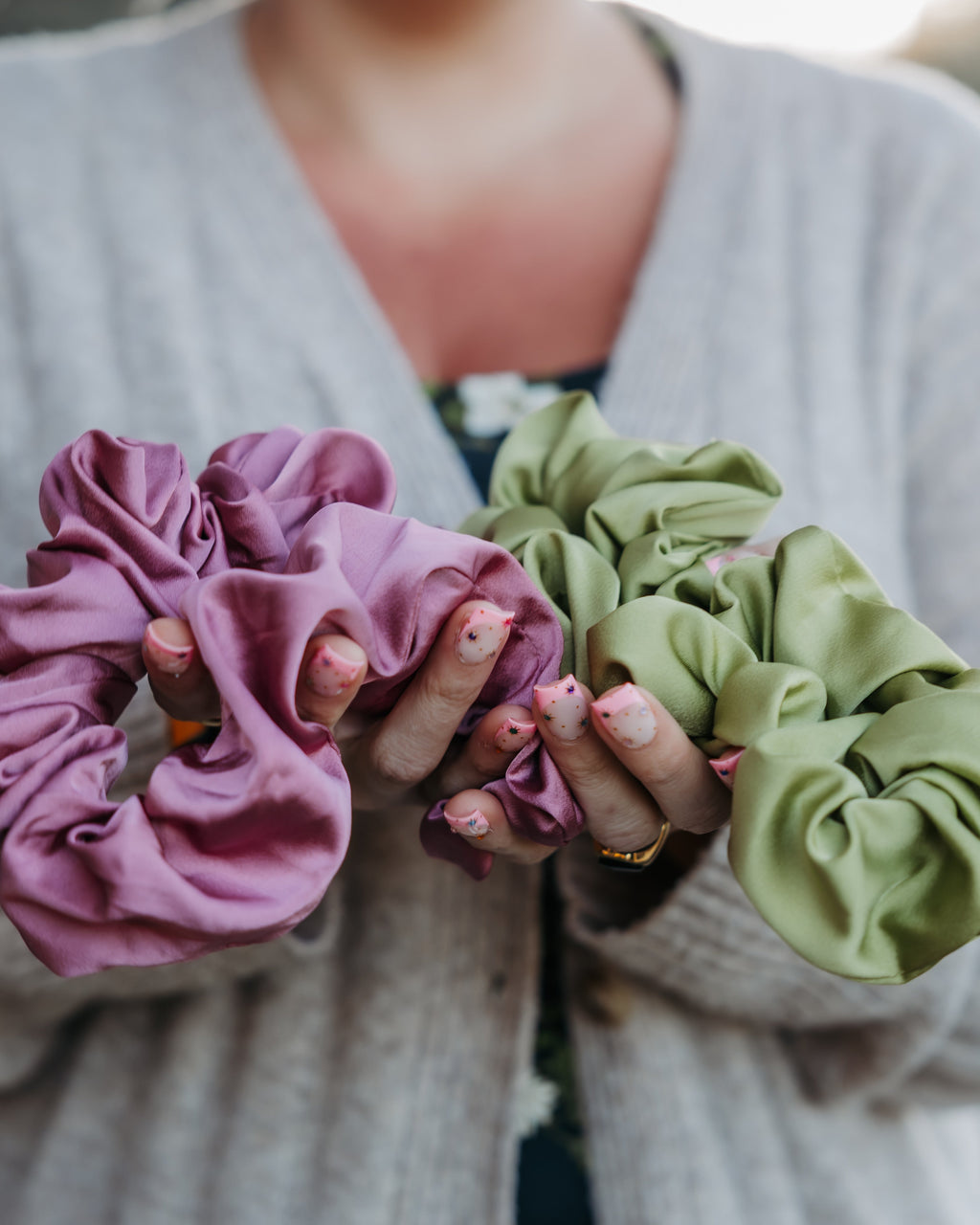 Person holding two scrunchies, one Hibiscus pink and one Kiwi green, outdoors.