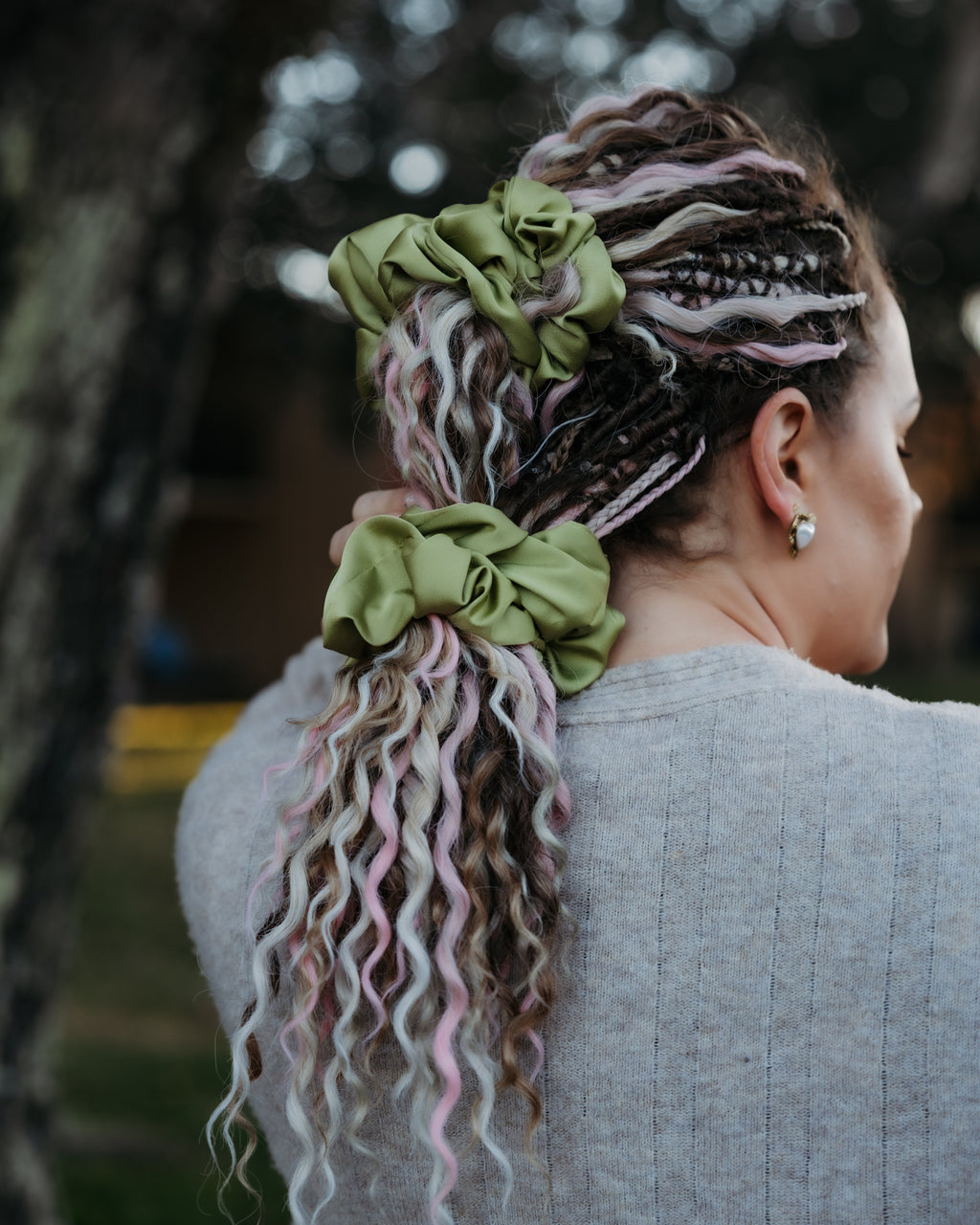 Person with colorful braided hair and green scrunchies, standing outdoors.