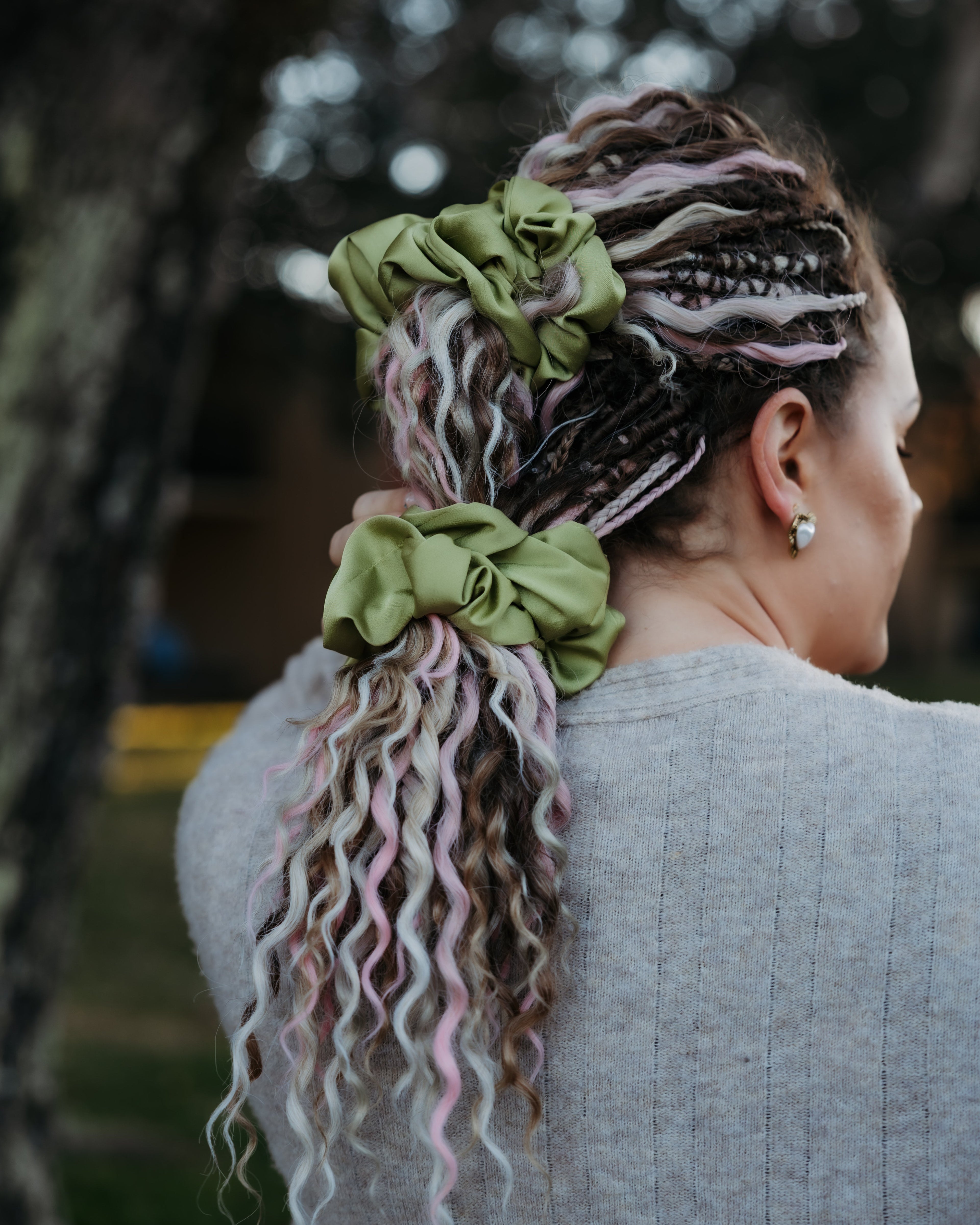 Person with colorful braided hair and green scrunchies, standing outdoors.