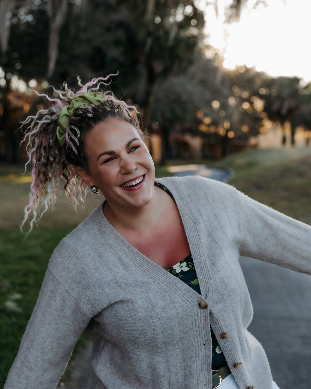 Woman in a gray cardigan standing outdoors with trees in the background