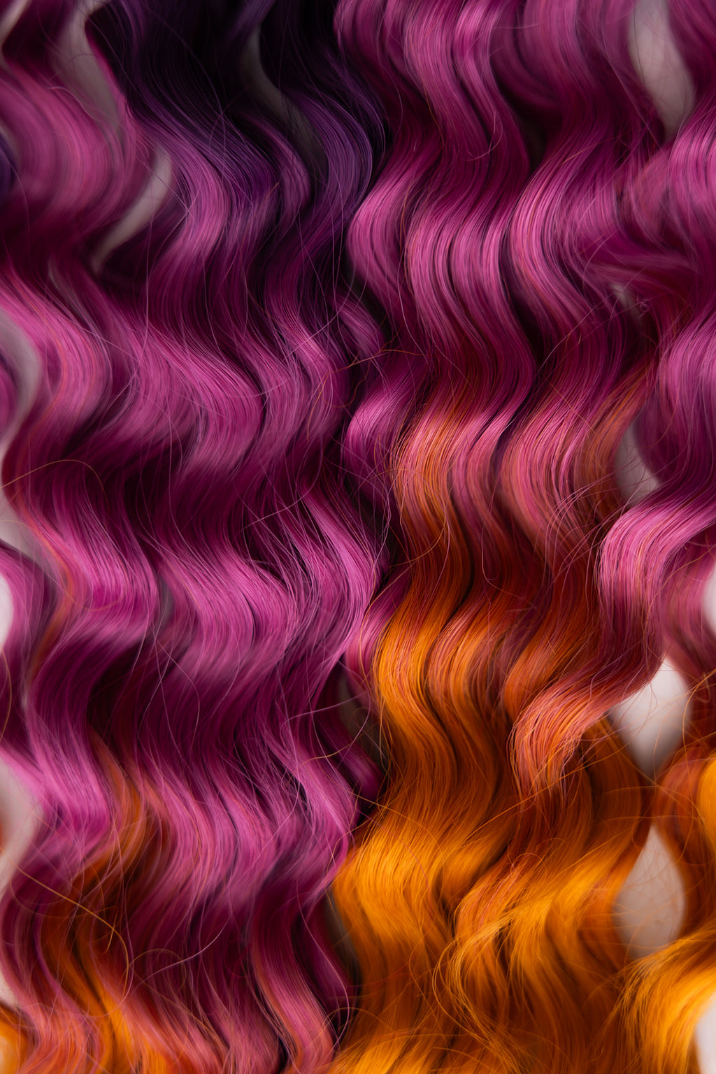 Close-up of wavy hair with a vivid color gradient transitioning from deep purple at the top to bright pink and orange at the bottom.